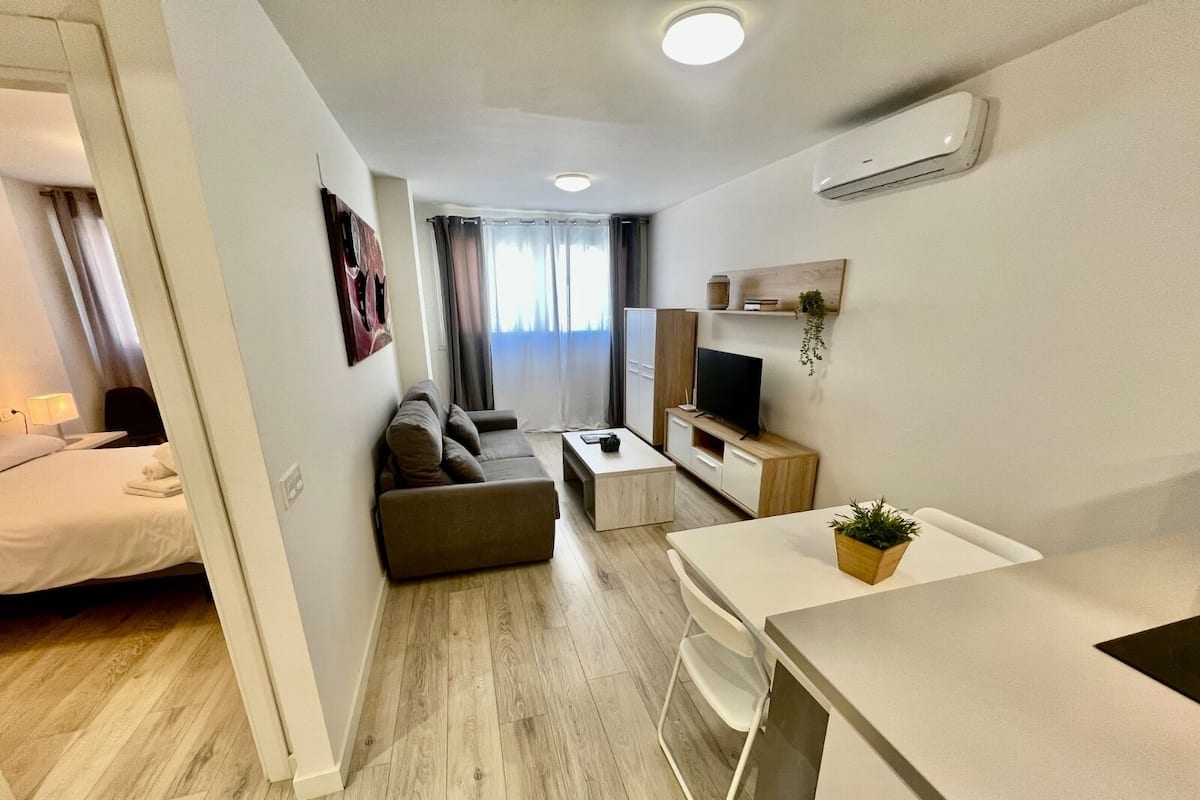 Una sala de estar moderna y bien iluminada con un sofá, un televisor y una mesita.