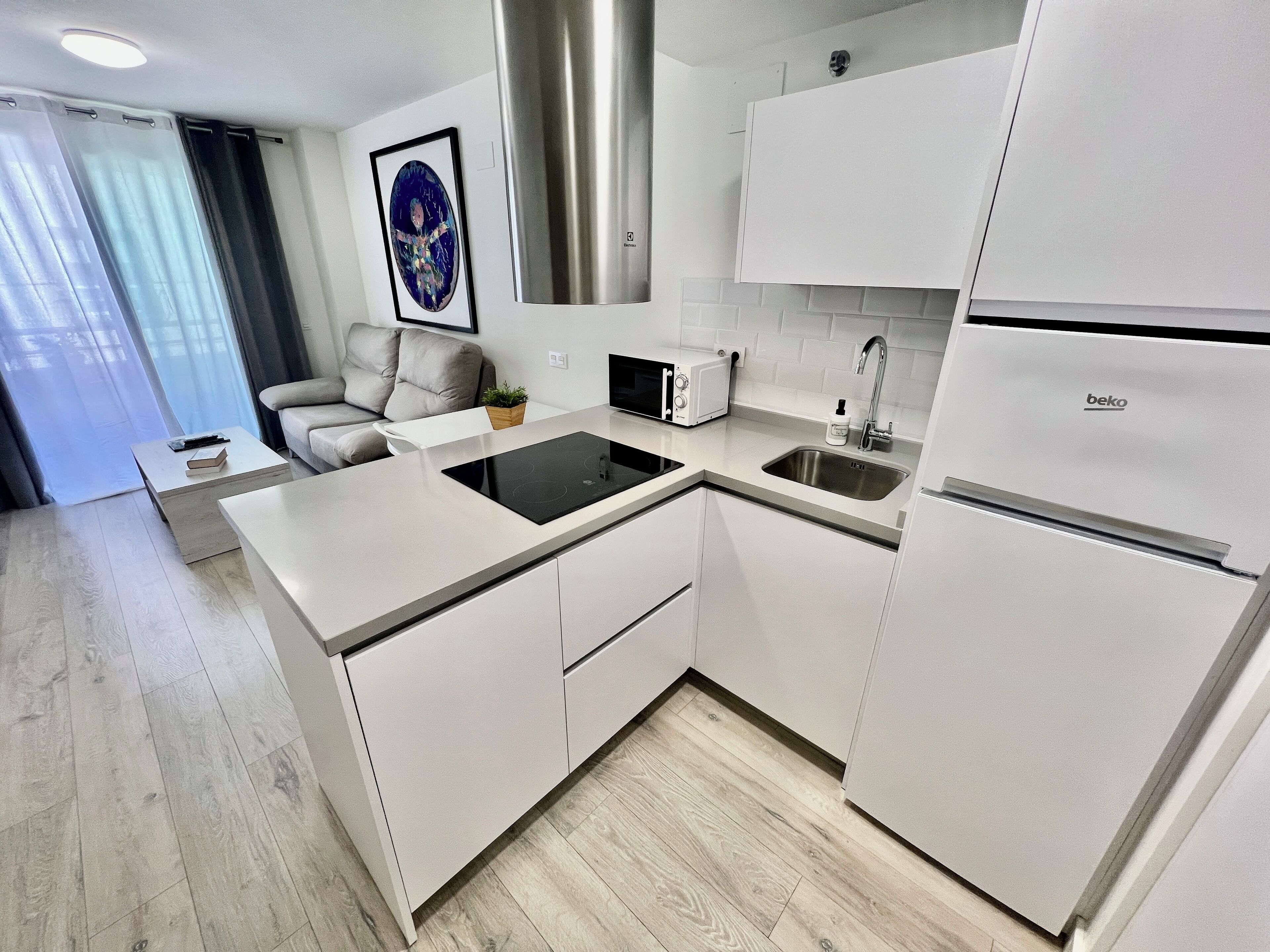 Una cucina moderna con mobili bianchi, forno a microonde integrato, lavello e cappa aspirante in acciaio inossidabile.
