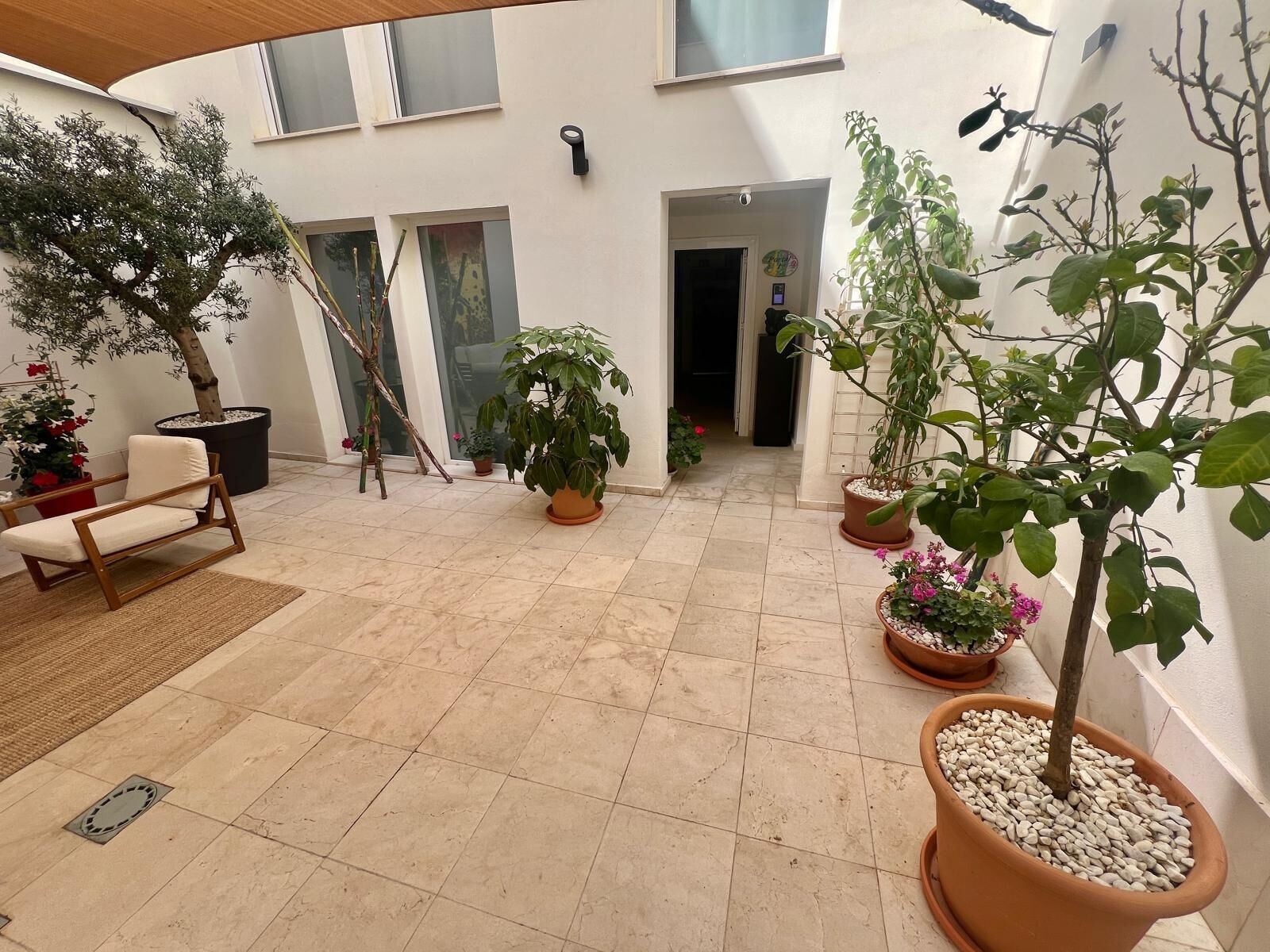 A spacious patio with tiled flooring, several potted plants, a wooden chair, and a door leading to an interior space.