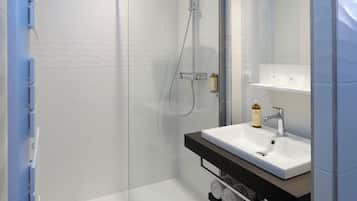Un baño moderno con ducha de vidrio, lavamanos blanco y espejo sobre él.