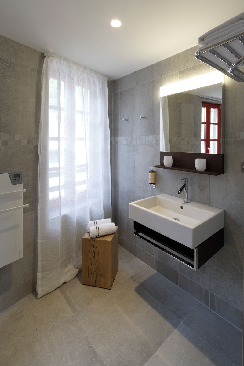 A modern bathroom with a large mirror, a white sink, and a wooden stool.