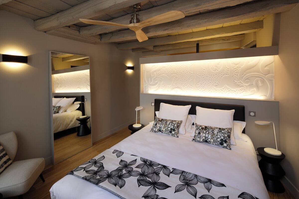 A modern bedroom with a large bed, two bedside tables, a ceiling fan, and a mirror.
