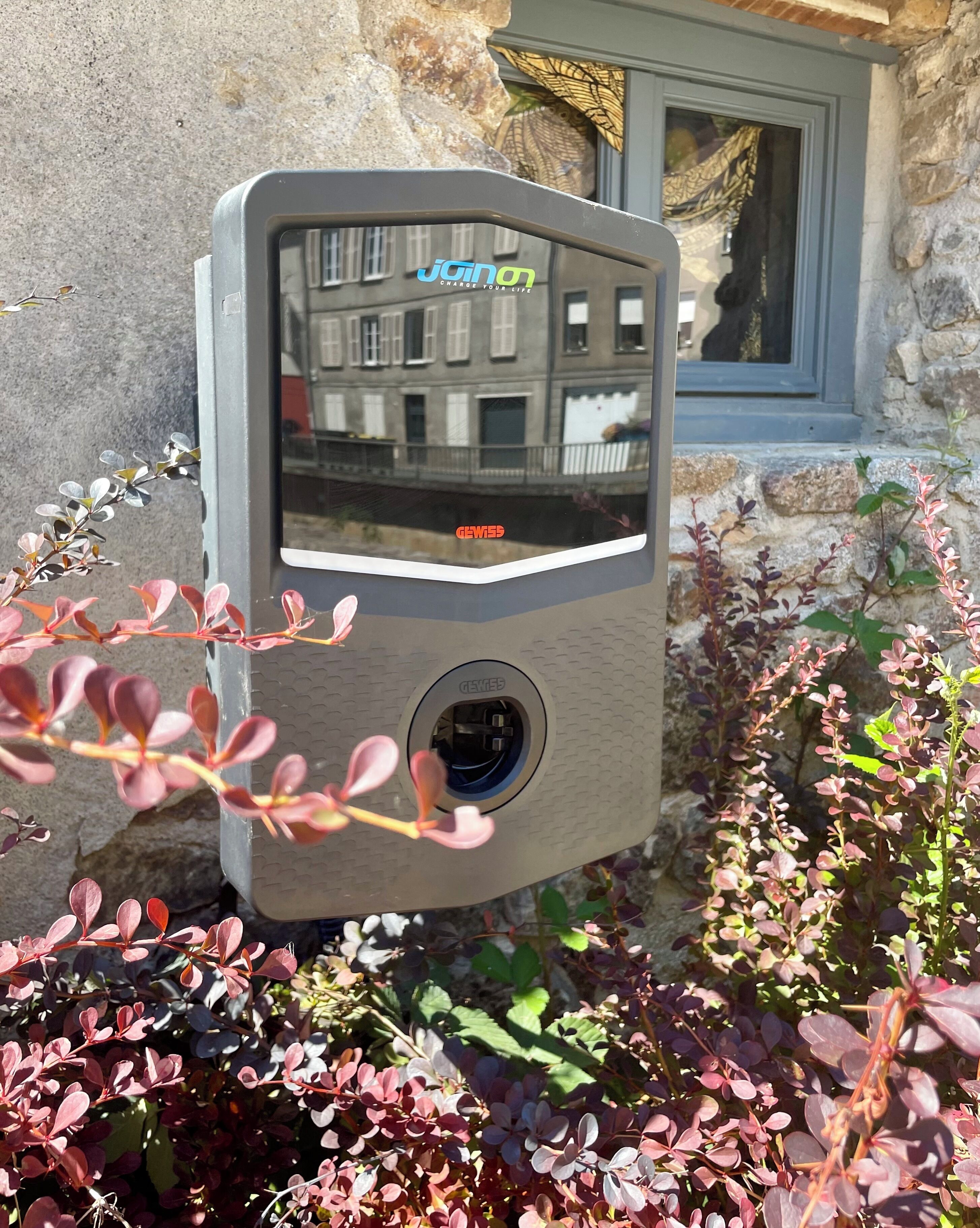 Cámara de seguridad fijada en una pared de piedra, con una ventana y plantas al frente.