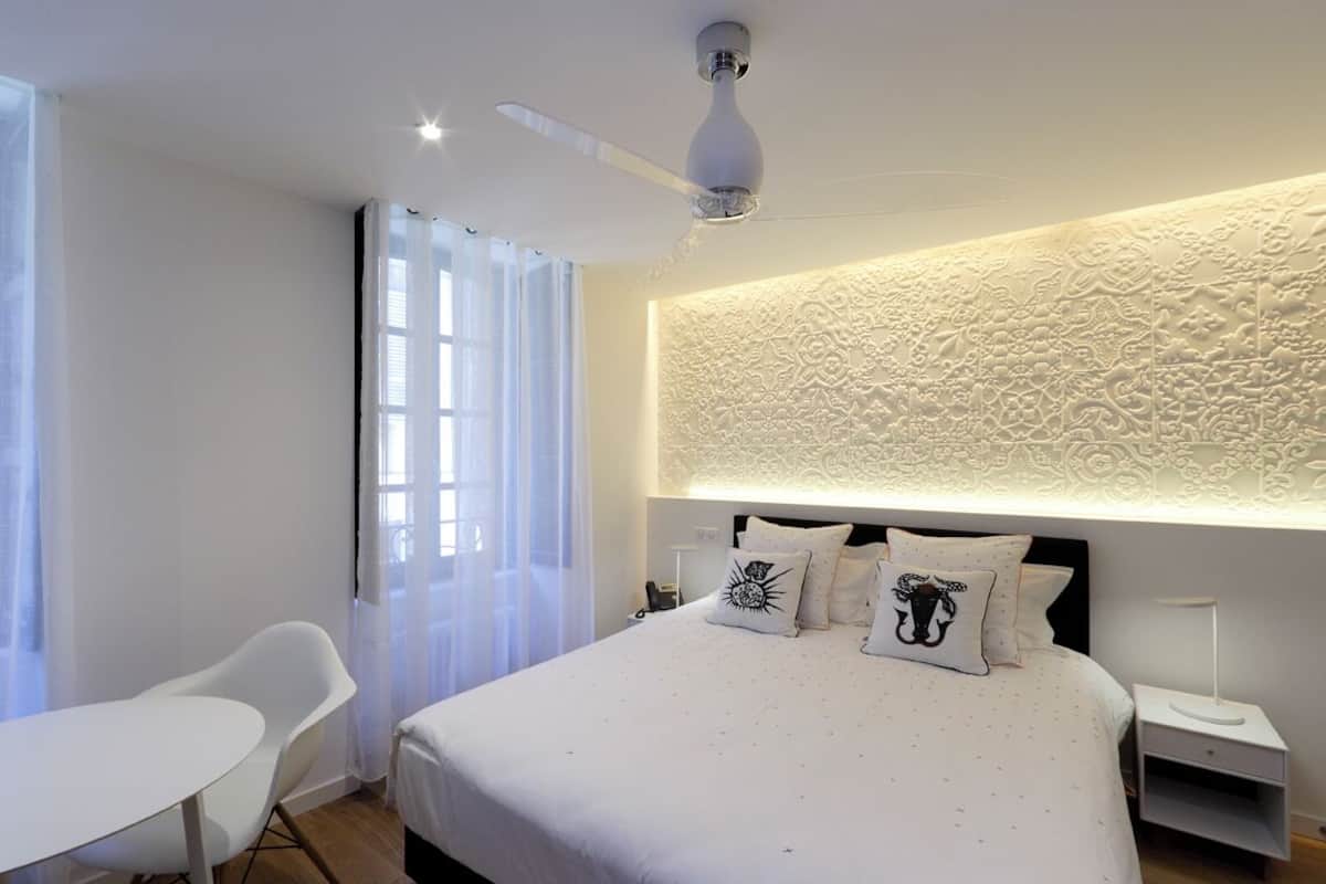 A modern hotel room with a large bed, a desk, and a ceiling fan.