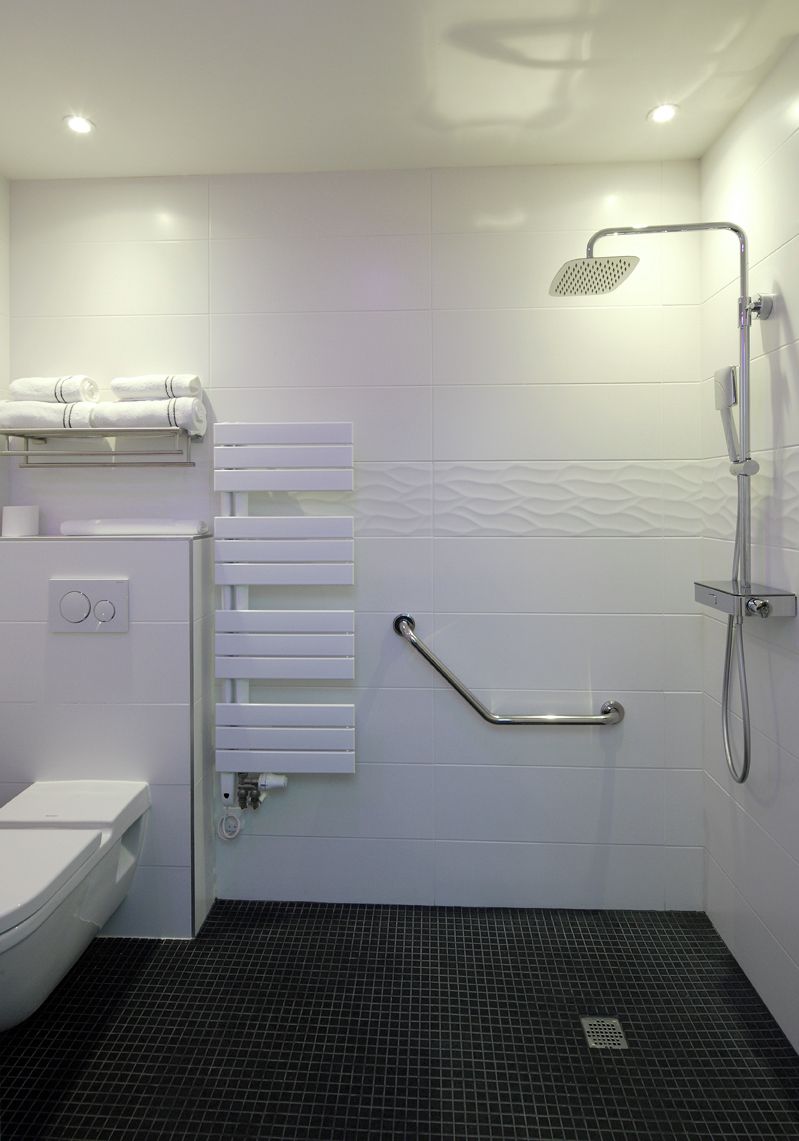 A modern bathroom with a toilet, a towel rack, a heated towel rail, a grab bar, and a shower with a handheld showerhead.