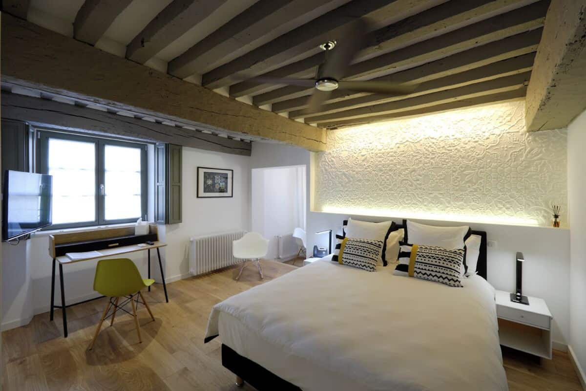 A bedroom with a bed, a desk, a chair, and a window.