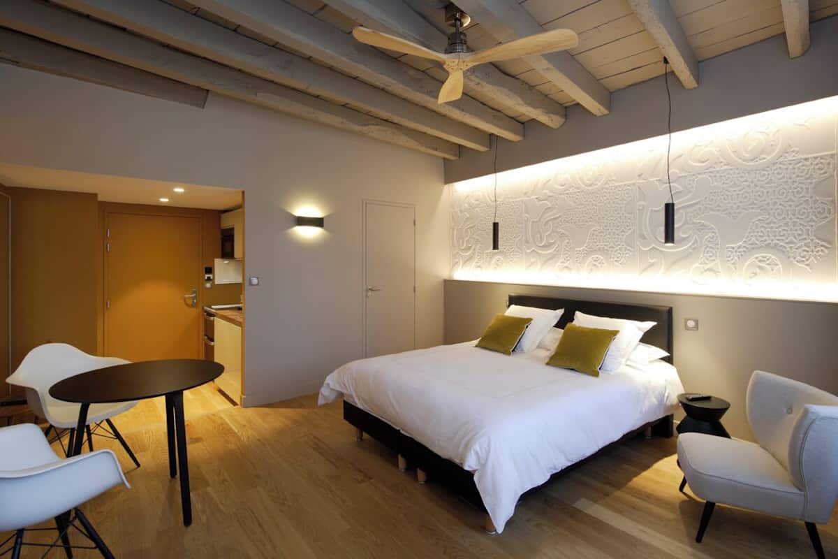 A modern bedroom with a large bed, a dining table, and a ceiling fan.