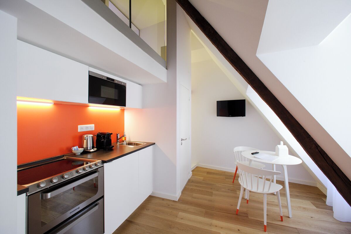 A modern kitchen with a built-in oven and microwave, a dining area with a white table and chairs, and a TV mounted on the wall.