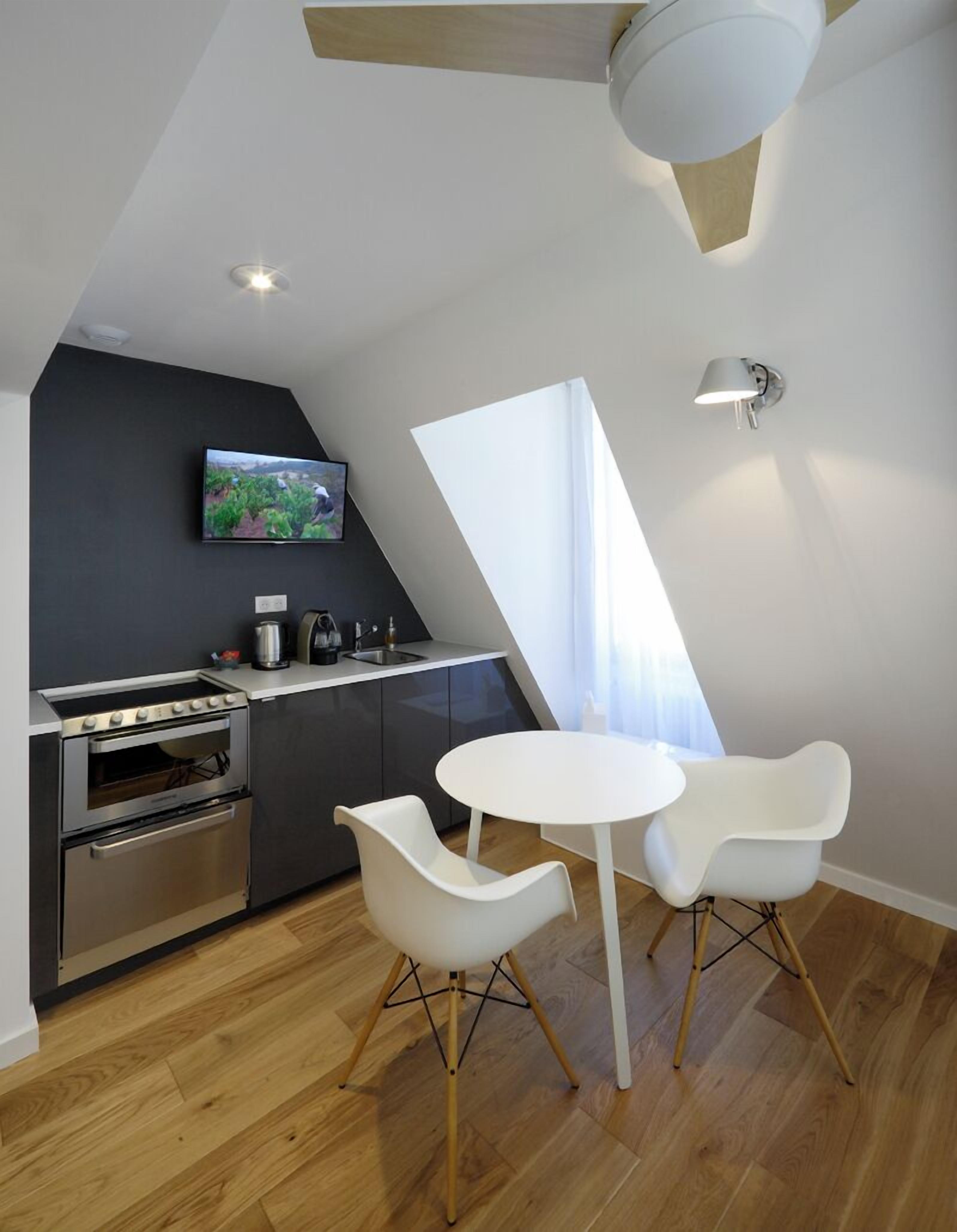 A modern kitchen with a built-in oven, a dining table with two chairs, and a television mounted on the wall.