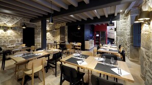 A restaurant with wooden tables and chairs, stone walls, and hanging pendant lights. - Les Maisons du pont - Charme & Caractère (Aubusson)