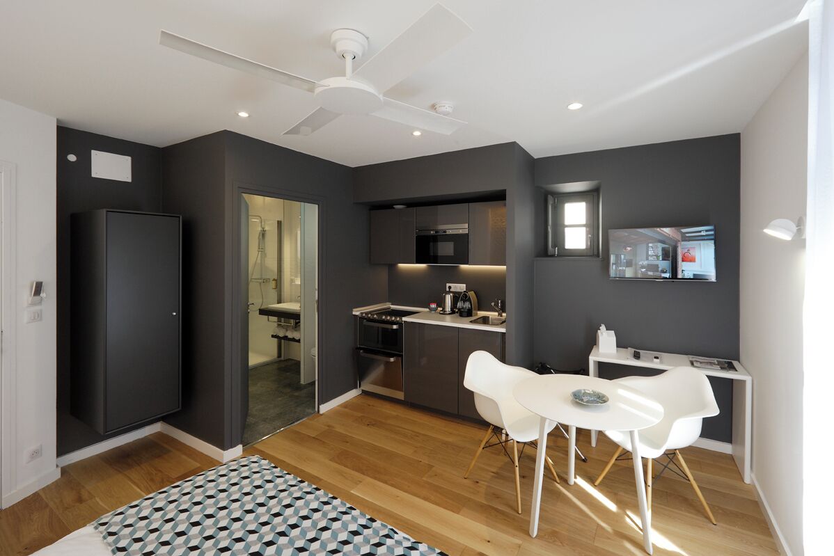 Een moderne keuken met donkere muren, een witte plafondventilator, en een eethoek met witte stoelen en een kleine tafel.