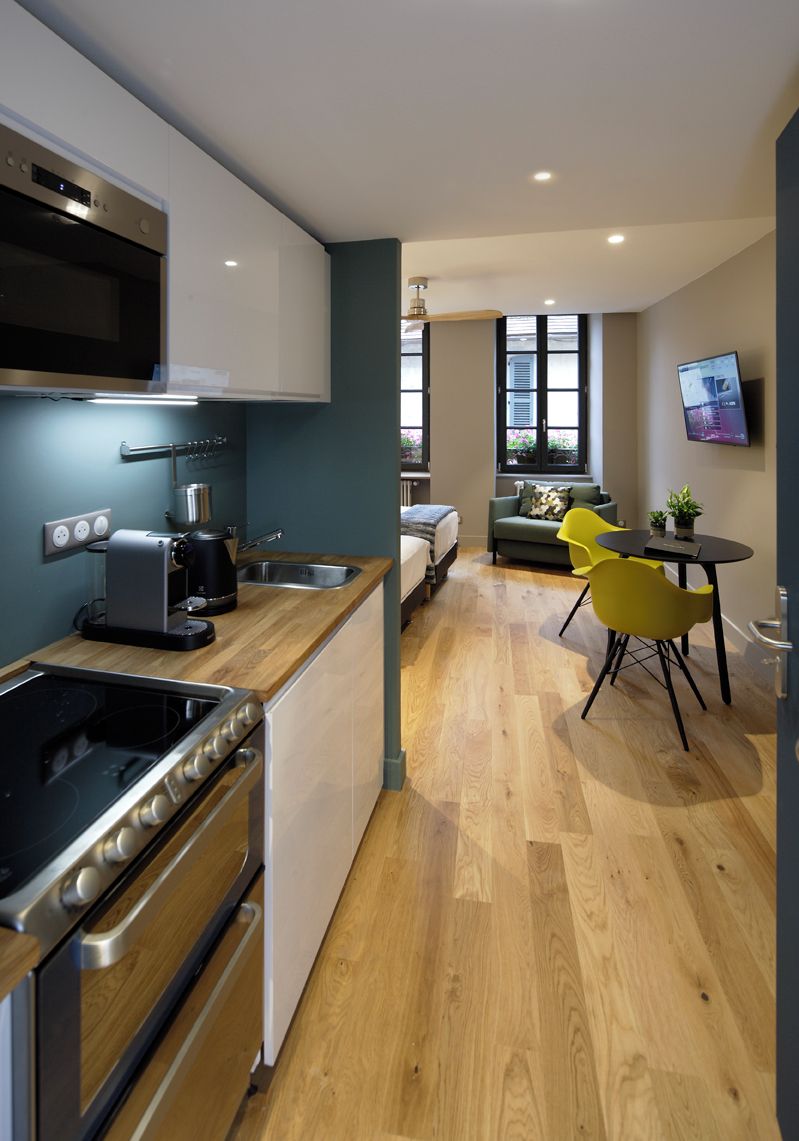 A modern kitchen with a built-in oven, microwave, and coffee maker. There is a dining area with yellow chairs and a small table.