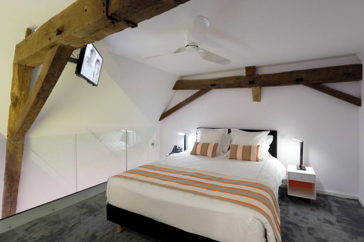 A bedroom with a bed, a ceiling fan, a nightstand, and a TV mounted on the wall.