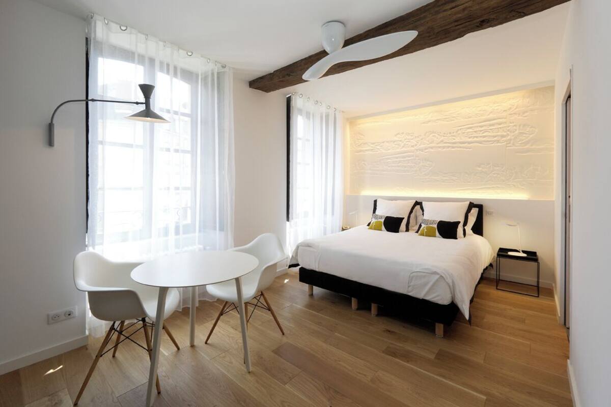 A modern hotel room with a bed, a desk, two chairs, and a ceiling fan.