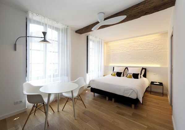 Una habitación de hotel moderna con cama, escritorio, dos sillas y ventilador de techo.