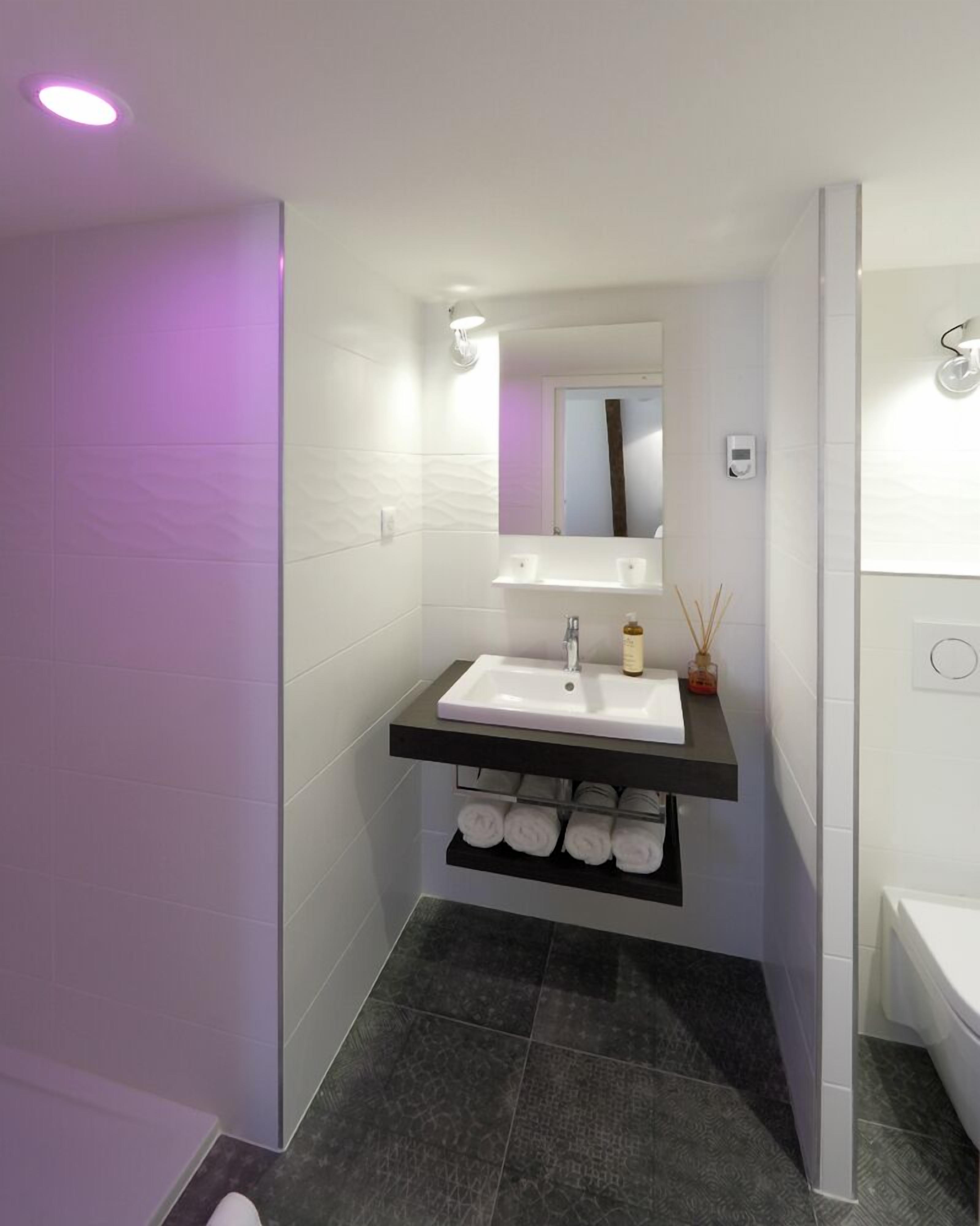 A modern bathroom with a white sink, a mirror above it, and a shelf below holding towels.