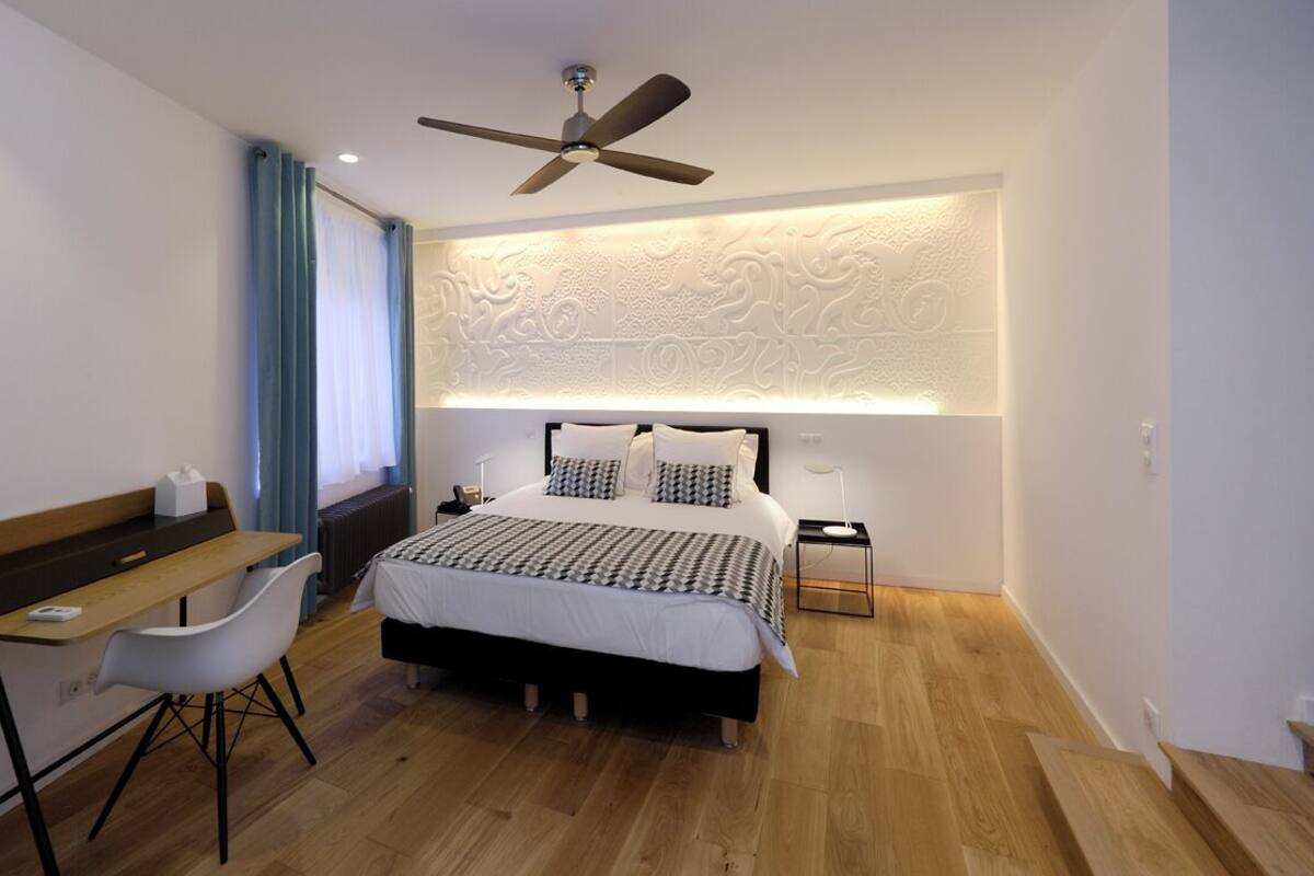 A modern bedroom with a bed, desk, chair, and a ceiling fan.