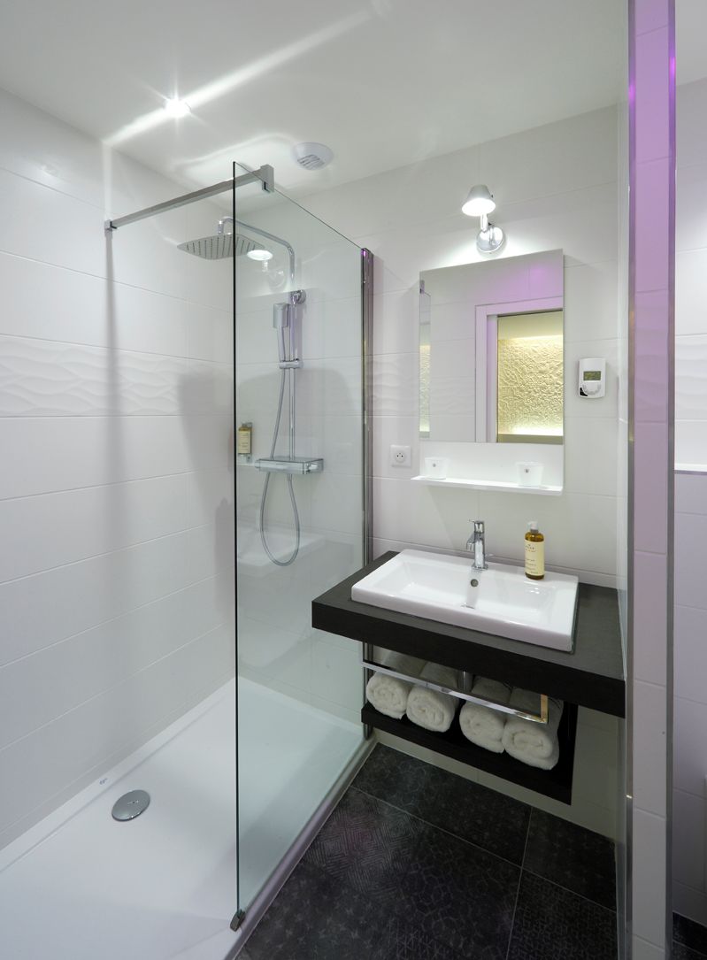 A modern bathroom with a glass-enclosed shower, a white sink with a black countertop, and a mirror with a gold-framed inset.