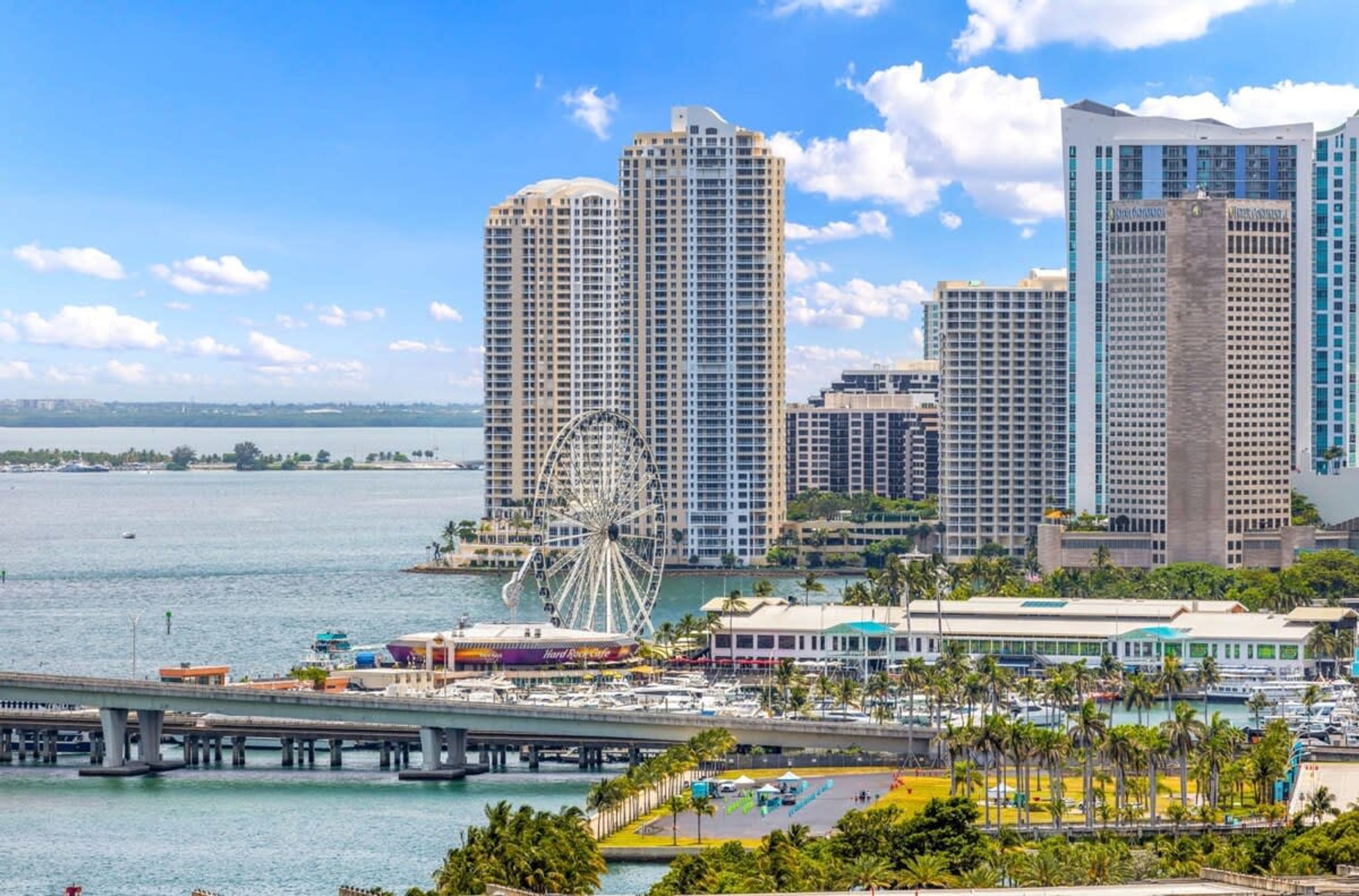 A waterfront cityscape with high-rise buildings, a Ferris wheel, and a marina.
