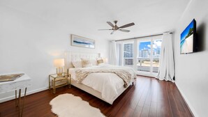 A bedroom with a bed, a ceiling fan, a window with curtains, and a view of buildings. - Florida Sunrise Pool Hot Tub (Miami)
