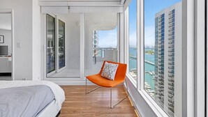 A modern hotel room with a large balcony, a bed, a chair, and a view of a marina and buildings. - Highrise Charm (Miami)