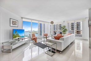 A modern living room with a large TV, white furniture, and a view of the city.