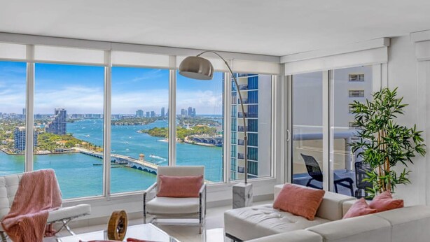 A modern living room with a large window overlooking a marina and city skyline. - Highrise Charm (Miami)