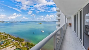 Uma varanda com vista para um mar calmo, céu claro e um horizonte urbano distante.