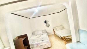 Una stanza compatta dalle pareti bianche, con un letto, un tavolino e una sedia.