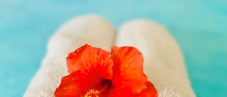 Dos toallas blancas dobladas con orden y una flor de hibisco rojo encima.