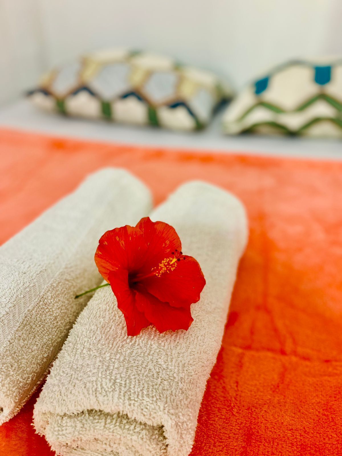 Two white towels with a red hibiscus flower on one, placed on an orange towel.