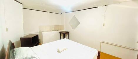 Una habitación pequeña y limpia con una cama, una mesita y una kitchenette.