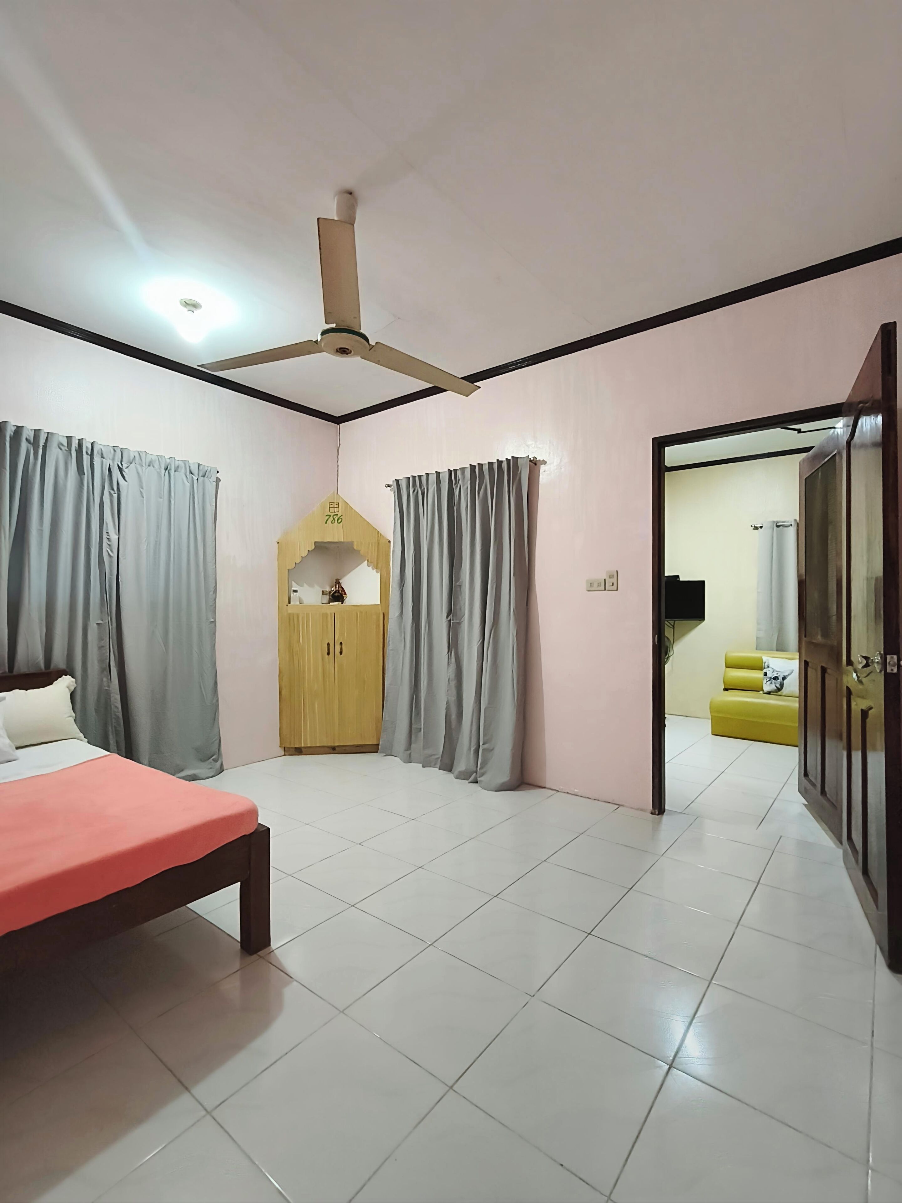 A bedroom with a bed, a ceiling fan, a wardrobe, and a view into another room with a sofa.