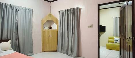 A bedroom with a bed, a ceiling fan, a wardrobe, and a view into another room with a sofa.