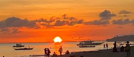 A beach scene at sunset with boats and people.