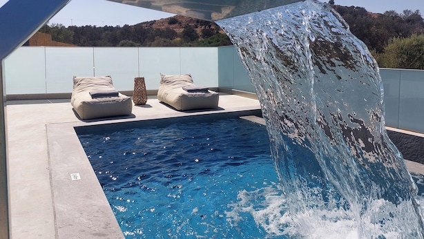 Una piscina con cascada, sillas de descanso y vistas del paisaje circundante.