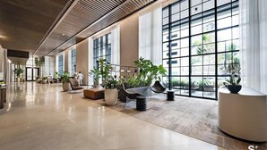 Un vestíbulo amplio con ventanas grandes, zonas de estar y plantas en macetas.