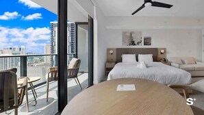 A modern hotel room with a large bed, a ceiling fan, a balcony with seating, and a city view.