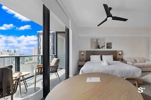 Habitación de hotel moderna con una cama grande, ventilador de techo, balcón con asientos y vista a la ciudad.