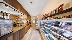 A modern cafe with a counter, refrigerated display, and shelves stocked with snacks and beverages.