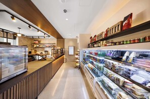 Un café moderno con mostrador, vitrina refrigerada y estantes llenos de refrigerios y bebidas.