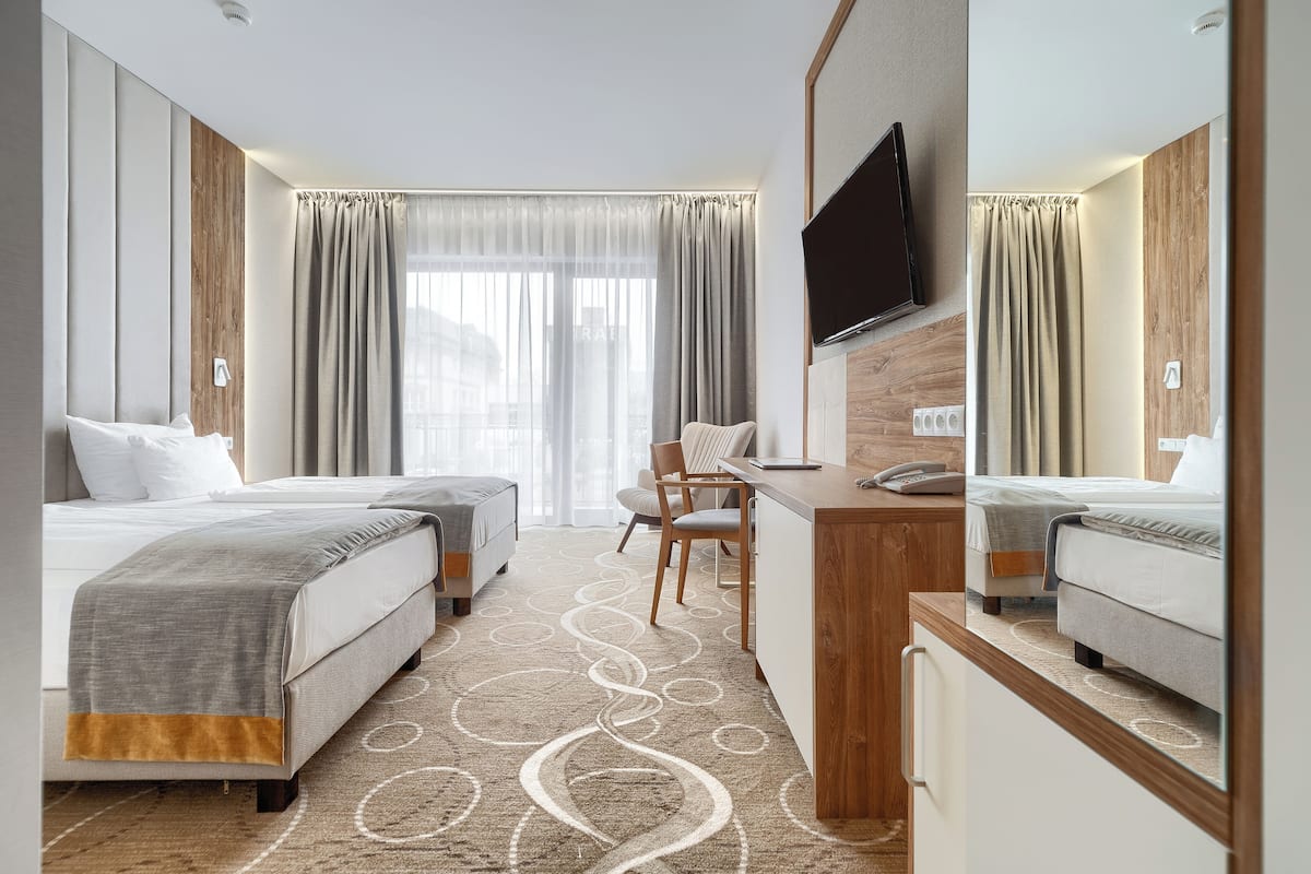 Een hotelkamer met twee bedden, een bureau, een stoel, een televisie en een groot raam met gordijnen.