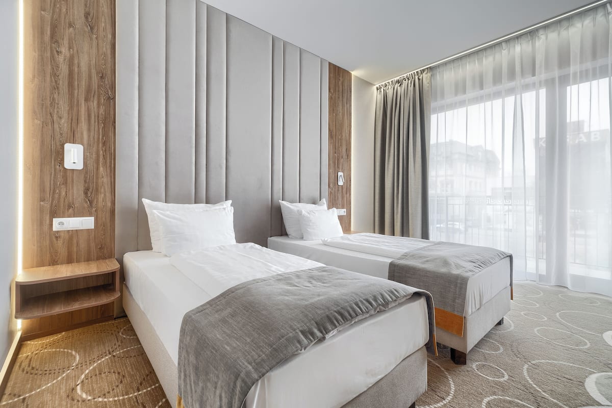 Een hotelkamer met twee bedden, een houten accentmuur, een groot raam met gordijnen en uitzicht op gebouwen.