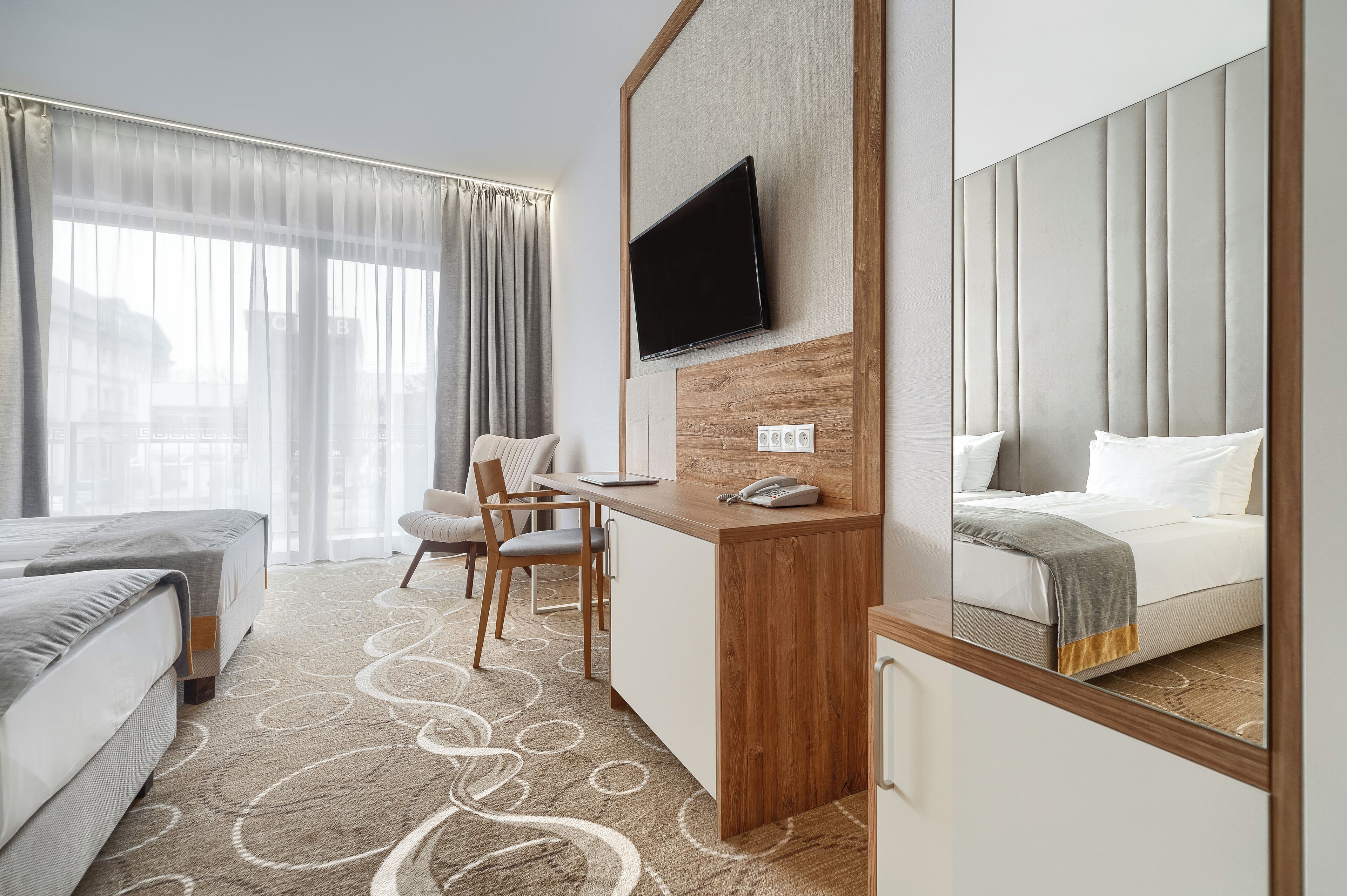 Ein Hotelzimmer mit Bett, Schreibtisch, Stuhl, Wand-TV und einem großen Spiegel.