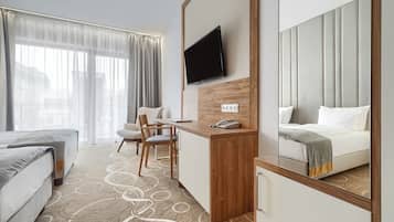 A hotel room with a bed, a desk, a chair, a TV mounted on the wall, and a large mirror.