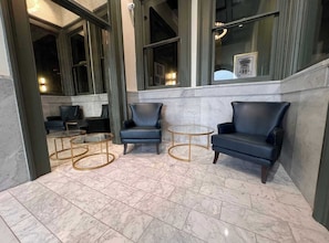 A lobby with marble flooring, two black leather armchairs, a glass coffee table, and a round table with gold legs.
