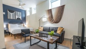 Et moderne hotelværelse med seng, sofa, sofabord og fjernsyn.