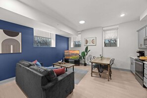 En moderne stue med en grå sofa, et træspisebord og et køkkenområde med mikrobølgeovn og ovn.