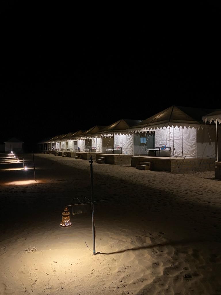 A row of tents with a sandy ground, a metal pole, and a lantern.