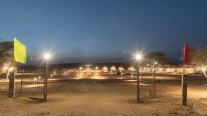 A well-lit outdoor area with a sandy ground, metal fencing, and flags. - Tokyo Desert Camp (Jaisalmer)